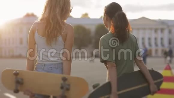 两个少女朋友在阳光下玩滑板在欧洲街镇嘲笑外面的东西的肖像视频的预览图