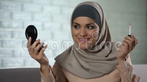 漂亮的阿拉伯家庭主妇涂着唇彩照着小镜子美丽时尚视频的预览图