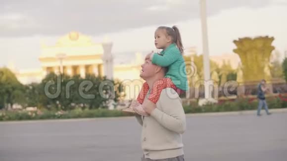 可爱的小女儿骑在肩膀上父亲在夏天的城市公园散步视频的预览图
