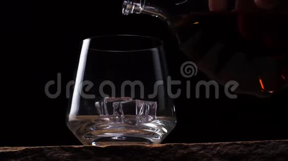 瓶子被倒入一杯黑背景带冰的威士忌中视频的预览图