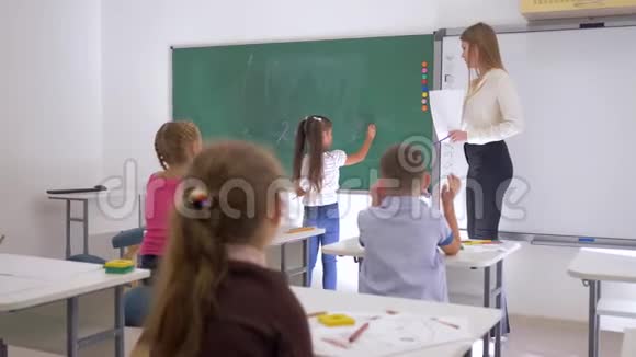 女学生在教师旁边的黑板上写了一个简单的例子数学课小学教育视频的预览图