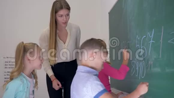 在学校的一节课上教育工作者用粉笔帮助孩子们在黑板上书写字母和数字视频的预览图