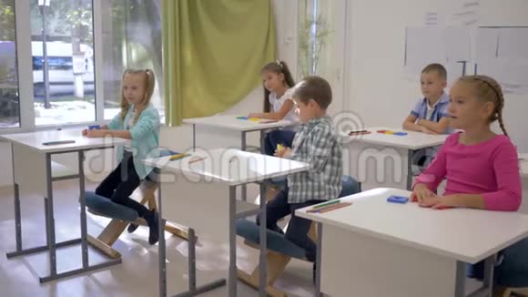 学校里的孩子们男孩和女孩坐在课桌前在课堂上举手视频的预览图