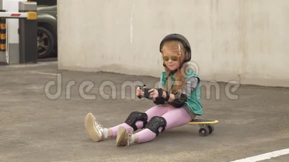 开朗的小女孩坐在黄色的滑板上正在使用手机上网冲浪视频的预览图