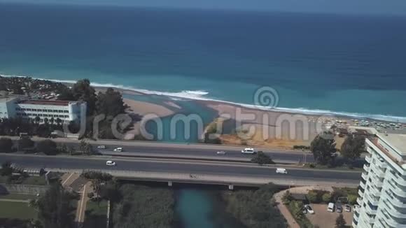 在温暖的夏日里在靠近大海的道路上行驶的汽车和站在斜坡上的豪华酒店的空中景观剪辑视频的预览图