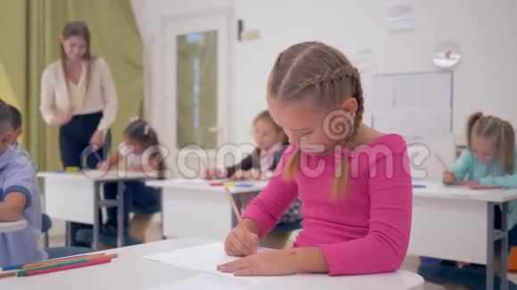 女学生用铅笔在纸上画画然后微笑着看着摄像机在灯光下的教室里上课视频的预览图