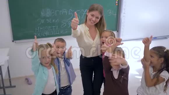 快乐的小学生老师在教室里以黑板为背景竖起大拇指视频的预览图