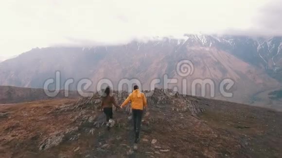 一对年轻的旅行者在群山的背景下举起双臂视频的预览图
