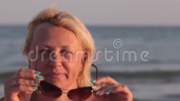 微笑的女人看着镜头在海浪的背景下戴上眼镜视频的预览图