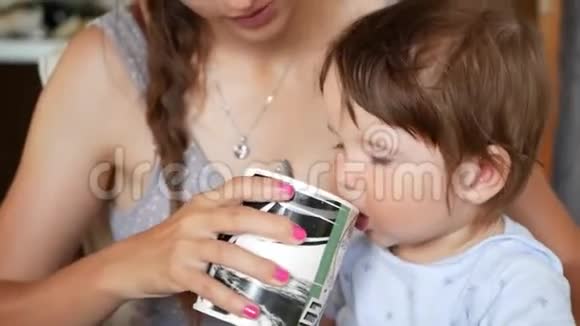 妈妈喂宝宝看手机一位抱着一个小孩子的年轻母亲拿着一部智能手机看着她视频的预览图
