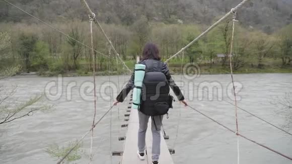 女孩旅行者带着背包在悬索桥上过河木头渡船过河女徒步旅行者视频的预览图