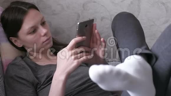 睡懒觉的女人躺在沙发上用手机读东西视频的预览图