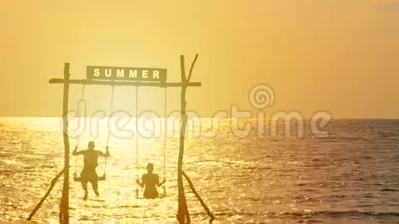 4K幸福夫妇的剪影喜欢在日落时间随着秋千在海上摇曳夏天的标志在上面快乐的夏天视频的预览图