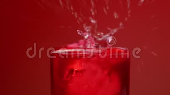冰块落在杯子里用红色苏打水溅起水花和气泡红色背景和慢动作视频的预览图