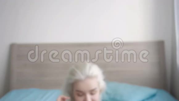 特写美丽的年轻金发女人醒来并在家的床上伸展视频的预览图