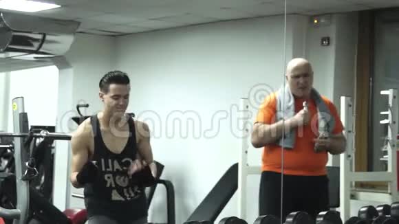 一个肥胖的滑稽男人和一个年轻英俊的运动员正在健身房跳舞视频的预览图