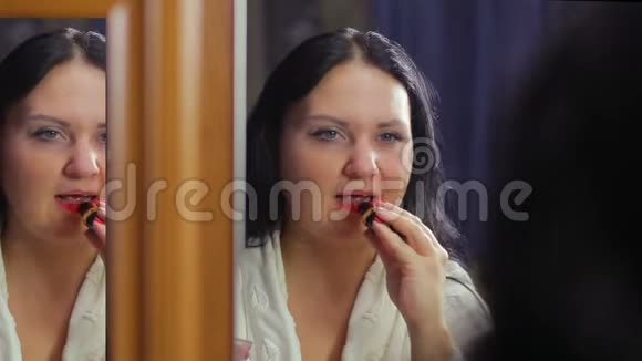 一个年轻的女人穿着一件白色的外套在镜子前用鲜红的口红包围着嘴唇视频的预览图