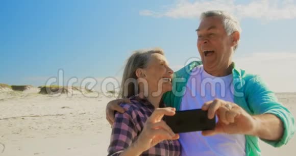 活跃的高加索夫妇在海滩上用手机自拍的正面景色视频的预览图