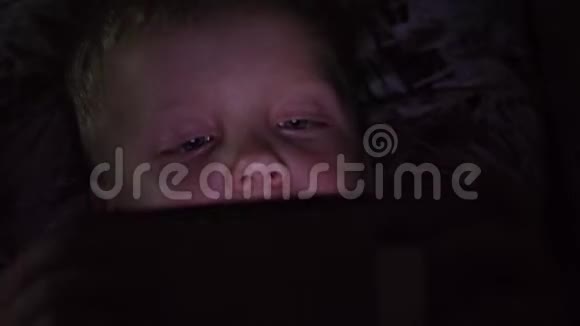 一个6岁的小男孩在黑暗的房间睡觉前看着智能手机视频的预览图