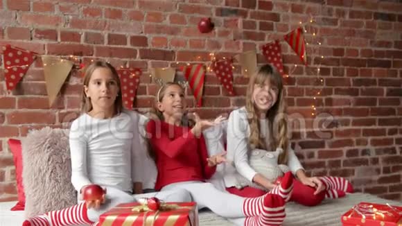 三姐妹穿着柔软的睡衣坐在床上玩着红苹果卧室装饰着圣诞节视频的预览图