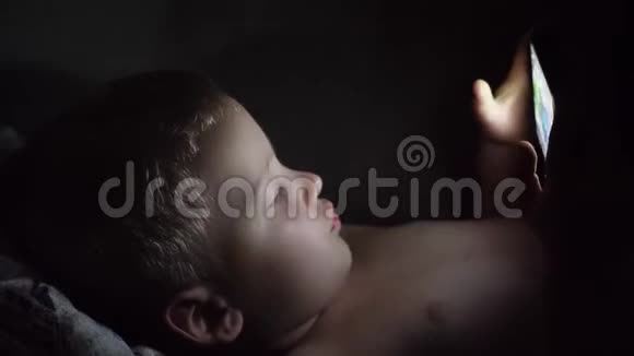 一个6岁的小男孩在黑暗的房间睡觉前看着智能手机视频的预览图