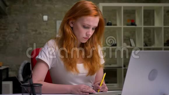 一位红发商务女性正努力工作在办公室里坐在笔记本电脑旁写着笔记本令人愉快视频的预览图