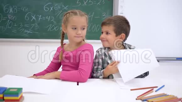 同学们抱着孩子微笑着坐在课桌前在教室里黑板的背景下视频的预览图