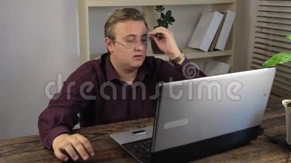 疲惫的商人戴着眼镜在办公室靠近笔记本电脑视频的预览图