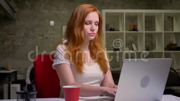 聪明的红发女郎正在笔记本电脑上打字正满怀信心地看着屏幕专心工作视频的预览图