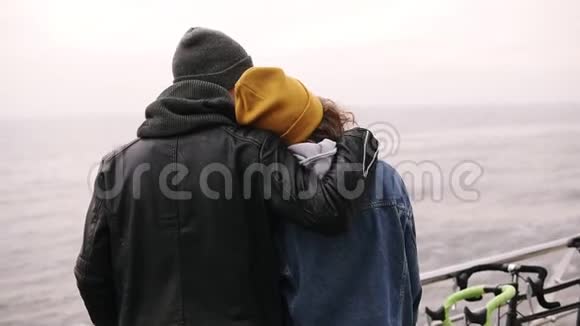 年轻人和一个女孩站在海上木墩上拥抱年轻夫妇享受时光戴着黄色帽子的女孩指着视频的预览图