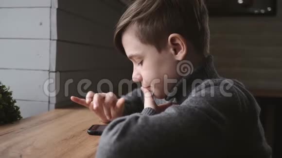 十几岁的男孩坐在窗边的咖啡馆里手里拿着一部智能手机社交网络中的交流运动会视频的预览图