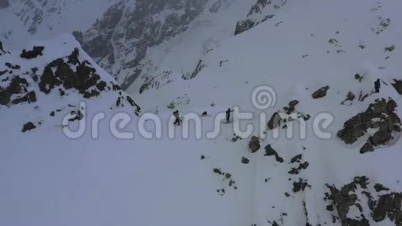 在暴风雪期间滑雪板上的人们在山上行走空中拍摄的4k镜头视频的预览图