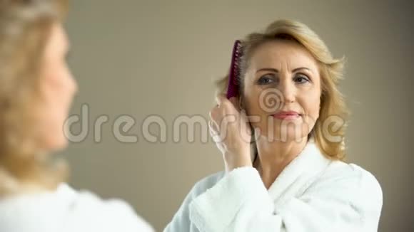 迷人的老年妇女在镜子前梳头微笑着老年美女视频的预览图