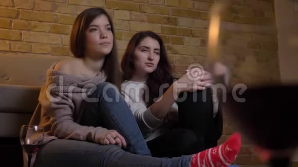 快乐的年轻白人女性朋友在舒适的家庭背景下看电视和拥抱的照片视频的预览图