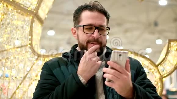 戴眼镜的胡子男看着智能手机读着留言视频的预览图