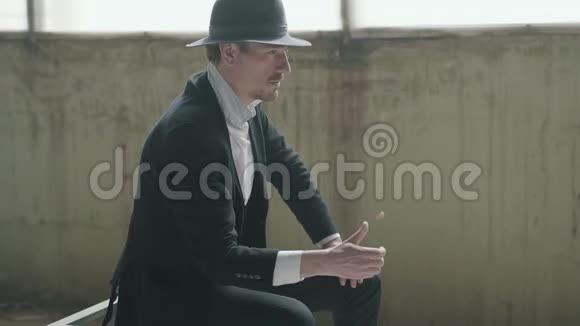 肖像英俊自信的男人戴着一顶帽子抛出并抓住硬币坐在一座废弃的建筑他的老板视频的预览图
