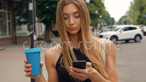 美丽的年轻女子走在城市里使用她的手机输入信息开心地笑美味的饮料视频的预览图