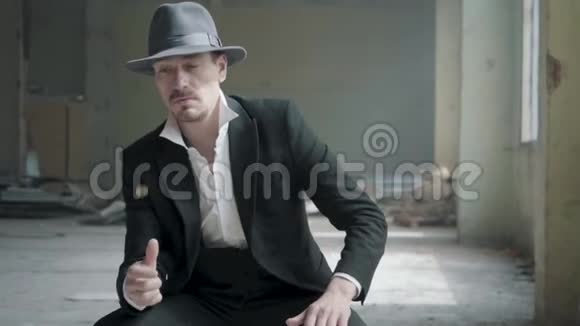 肖像英俊自信的男人戴着一顶帽子抛出并抓住硬币坐在一座废弃的建筑他的头视频的预览图