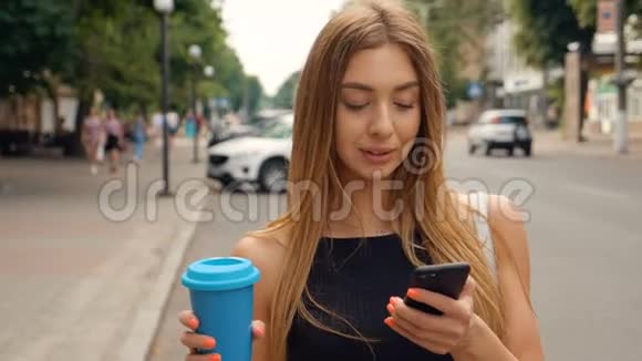 美丽的年轻女子走在城市里使用她的手机输入信息开心地笑美味的饮料视频的预览图