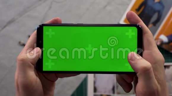 男人的特写镜头双手拿着智能手机背景衣柜里有一个水平的绿色屏幕准备着衣服视频的预览图