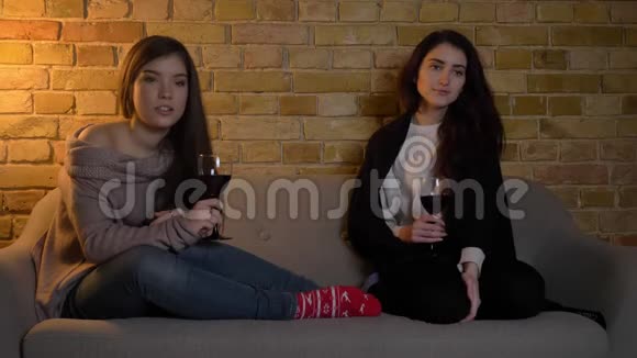 年轻的白种人女性朋友坐在沙发上端着酒杯在舒适的家里看电影视频的预览图