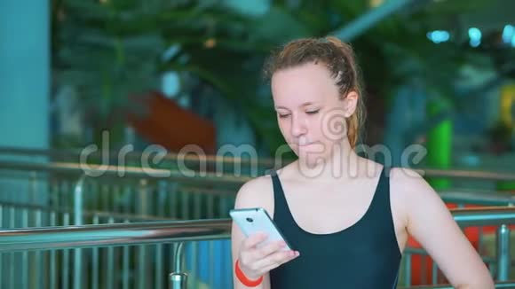 一个穿黑色泳衣的年轻女孩正在看你的智能手机视频的预览图