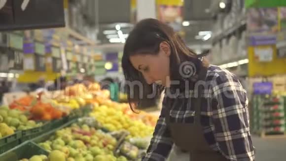 年轻漂亮的女店员穿着棕色围裙戴着白色手套在新鲜多汁的水果和梨子品种各种东西视频的预览图
