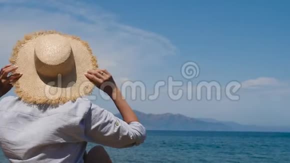 穿着衬衫戴着帽子的女孩坐在沙滩上的遮阳伞下视频的预览图
