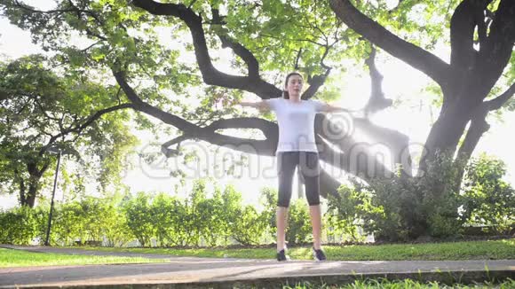 亚洲女人在花园里做跳跃的杰克有大树和阳光视频的预览图