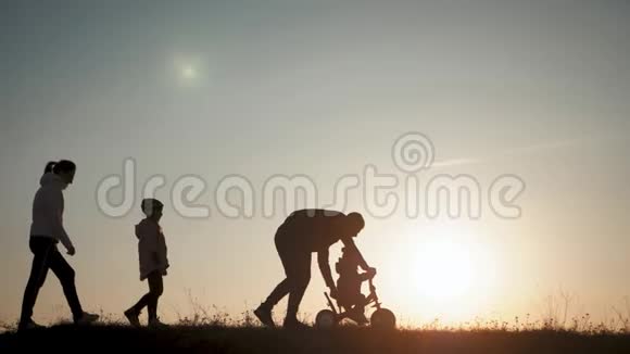 日落时分剪影一家人在一起小男孩学骑自行车爸爸教儿子骑自行车视频的预览图