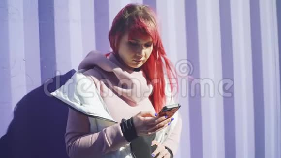 独立的年轻女性粉红色头发使用智能手机紫色容器背景慢动作视频的预览图