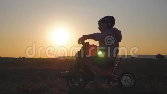 日落背景下骑自行车的女孩的剪影孩子在夕阳下玩自行车视频的预览图