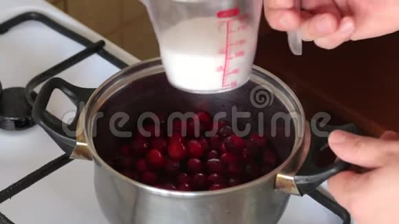 一个人把量杯中的糖加到平底锅中冷冻的蔓越莓中为棉花糖准备土豆泥视频的预览图