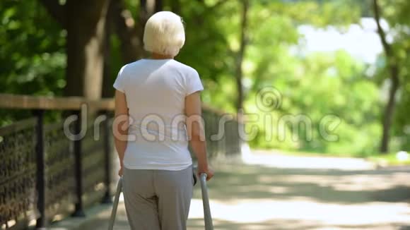老年妇女在康复中心公园用步行架移动后景视频的预览图